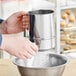 A person using the Fox Run stainless steel sifter to pour powdered sugar into a bowl.