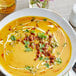 A bowl of soup with herbs and spices with a spoon on a table.