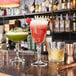 Arcoroc coupe glasses filled with colorful drinks on a bar counter.