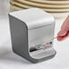 A hand using a Tablecraft toothpick dispenser on a white counter.