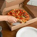 A hand slicing a pizza on a white pizza circle in a box.