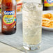 A glass of Goya Jamaican-style ginger beer with ice on a table next to a bottle of ginger beer.