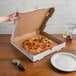 A person holding a 14" white corrugated pizza circle in a box.