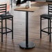 A square reversible laminated table top with a white birch and ash finish, mounted on a single black pedestal base.