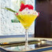 A Arcoroc martini glass filled with a yellow drink and a red fruit on top.