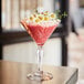 An Arcoroc martini glass on a table with a pink cocktail and flowers in it.