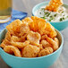 A bowl of Goya Chicharrones next to a bowl of dip with a crispy chip in it and a glass of beer.