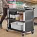 A woman pushing a black Choice utility cart with shelves and containers on wheels.