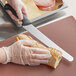 A person in gloves using a Mercer Culinary left-handed bread knife to cut a sandwich.