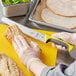 A person using a yellow Mercer Culinary Millennia bread knife to cut a sandwich.