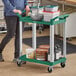 A woman pushing a green Choice utility cart with containers on it.