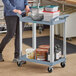 A woman pushing a gray Choice utility cart with containers on it.