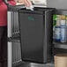 A woman using a black Choice refuse bin on a cart in a professional kitchen.