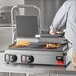 A man using a Vollrath Cayenne Double Panini-Style Sandwich Press to cook sandwiches in a professional kitchen.