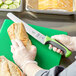 A person's hand holding a Mercer Culinary Millennia Colors bread knife and cutting a loaf of bread.