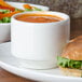 A Homer Laughlin Pristine Ameriwhite china bowl of soup next to a sandwich.