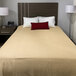 A bed with a tan Oxford Jaipur thermal honeycomb blanket and pillows in a hotel room.