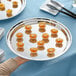 A person's hand holding an Acopa stainless steel catering tray of food.