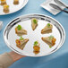A person's hand holding an Acopa stainless steel catering tray with food on it.