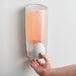 A hand pressing a Dial manual hand soap dispenser on a wall.