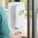 A person in a blue shirt using a Dial FIT universal touch-free hand sanitizer dispenser.