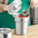 A woman using a Vollrath stainless steel ladle to pour red sauce into a silver container.