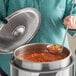 A woman using a Vollrath stainless steel ladle to serve soup from an inset pot.