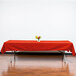 An orange Intedge rectangular cloth table cover on a table with a vase of flowers.