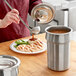 A woman using a Vollrath stainless steel container to pour sauce over food.