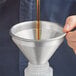 A person pouring liquid into an American Metalcraft aluminum funnel.