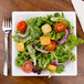 A salad with tomatoes, lettuce, and croutons in a WNA Comet white square Milan bowl.