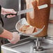 A person using a Choice aluminum gyro catch pan to cut a sandwich on a counter in a deli.