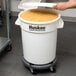 A person using a Continental Huskee white ingredient bin to hold yellow food.