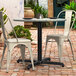 A black Lancaster Table & Seating outdoor table base with a white table and white chairs on a brick patio.