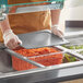 A person in a chef's uniform using a Vigor clear food pan with food in it on a counter in a salad bar.