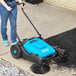 A person using a blue and black Lavex outdoor manual sweeper.