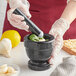 A person in gloves grinding basil and garlic in a Fox Run black marble mortar.