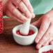 A person grinding red peppercorns in a white Fox Run mortar with a white pestle.