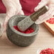 A gloved hand grinding red pepper in a Fox Run black granite mortar with a pestle.