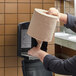 A man putting a Lavex Mini Center Pull Paper Towel Roll into a dispenser.