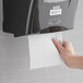 A hand using a white Lavex Select paper towel from a wall dispenser.