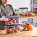 A woman in a chef's uniform holding a Vigor 6-pack of clear plastic food pans with secure sealing covers.