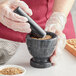 A person in gloves grinding seeds in a Fox Run marble mortar.