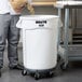 A man pouring grain into a large white Rubbermaid container with a lid.