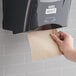 A hand using a Lavex Select natural kraft paper towel dispenser on a wall.