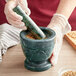 A person grinding seeds in a Fox Run green marble mortar with a pestle.