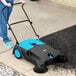 A woman using a blue and black Lavex outdoor manual sweeper.