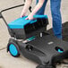 A woman using a blue and black Lavex manual sweeper to clean the floor.