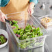 A person using a Vigor clear plastic food container to hold salad with a lid and drain tray.