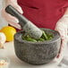 A person in gloves using a Fox Run black granite mortar to grind herbs.